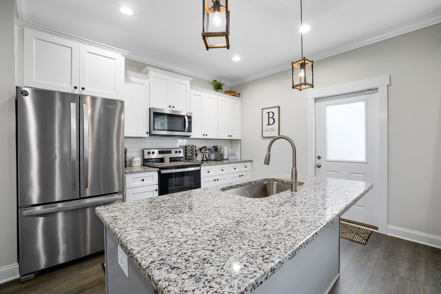 The renovated kitchen: white shaker cabinets, granite island, and stainless appliances